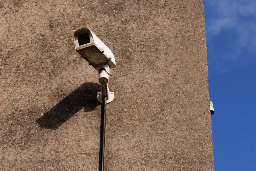 White bullet security camera on a concrete wall, its cable running down the wall inside a black conduit