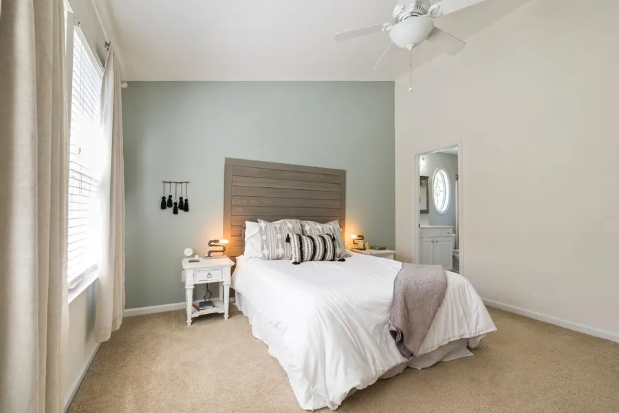 Bedroom with a sloped ceiling and a white ceiling fan with a light kit hung near the top of the slope