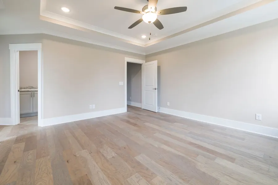 Empty room with a tray ceiling, a five-blade ceiling fan with a light kit in the centre and two recessed lights