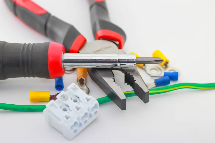 Screwdriver and wire stripping pliers on a white table with a green wire and a white terminal block