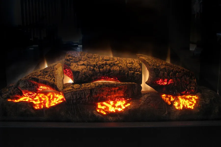 Close-up of an electric fireplace's artificial logs glowing orange and red inside a dark firebox