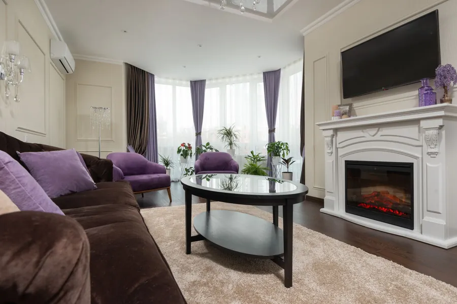 Living room with a white mantel around an electric fireplace insert and a flat-screen TV mounted on the wall above it