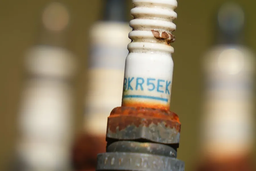 Close-up of a used spark plug with a rusted metal base, more worn plugs blurred behind it