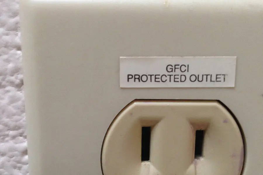 Close-up of an ivory outlet with a printed label above it that reads GFCI protected outlet
