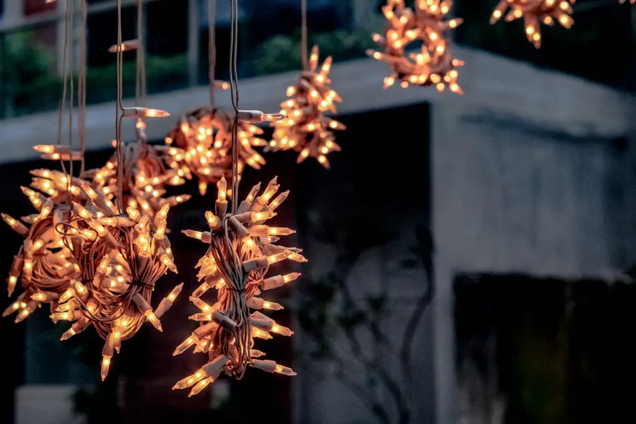 Bundles of warm incandescent mini-light strands glowing while they hang against a concrete building at dusk