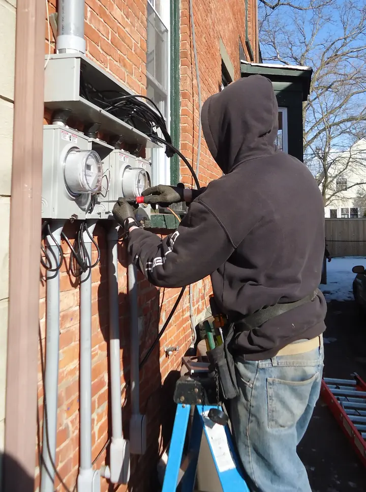 Electrician on a step ladder fitting new meter sockets to the brick wall of an older house