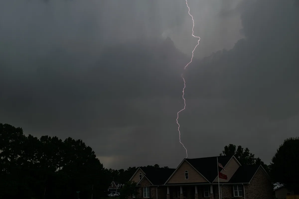 A lightning bolt under dark storm clouds above two-story suburban houses