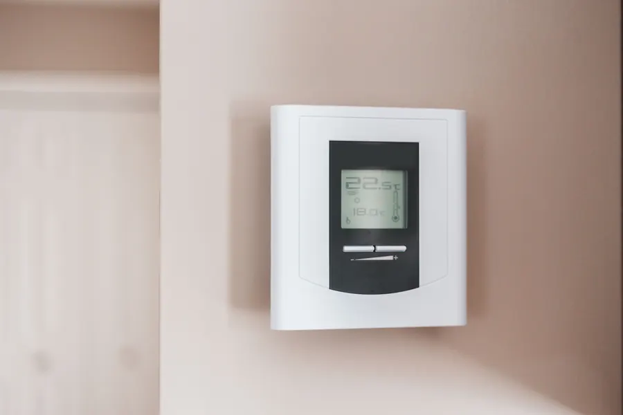 White digital wall thermostat with a gray display panel showing the room temperature