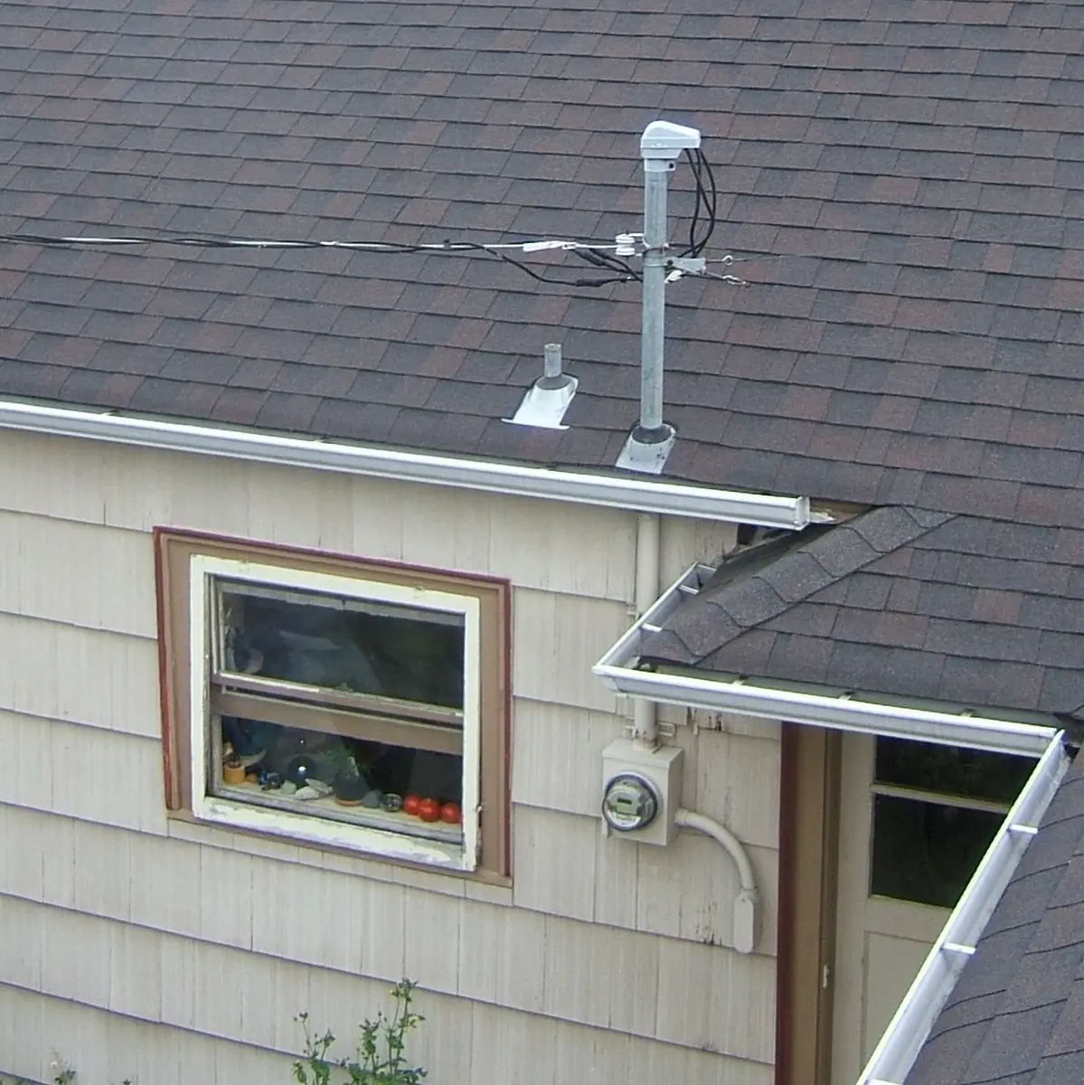 Photo of a utility service drop running to a steel mast through a shingle roof, with the electric meter mounted on the siding below