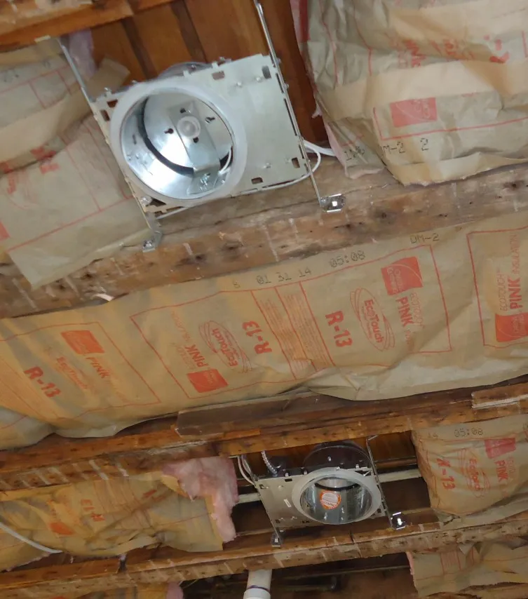 Two recessed light housings between ceiling joists, with pink fiberglass insulation held back from them