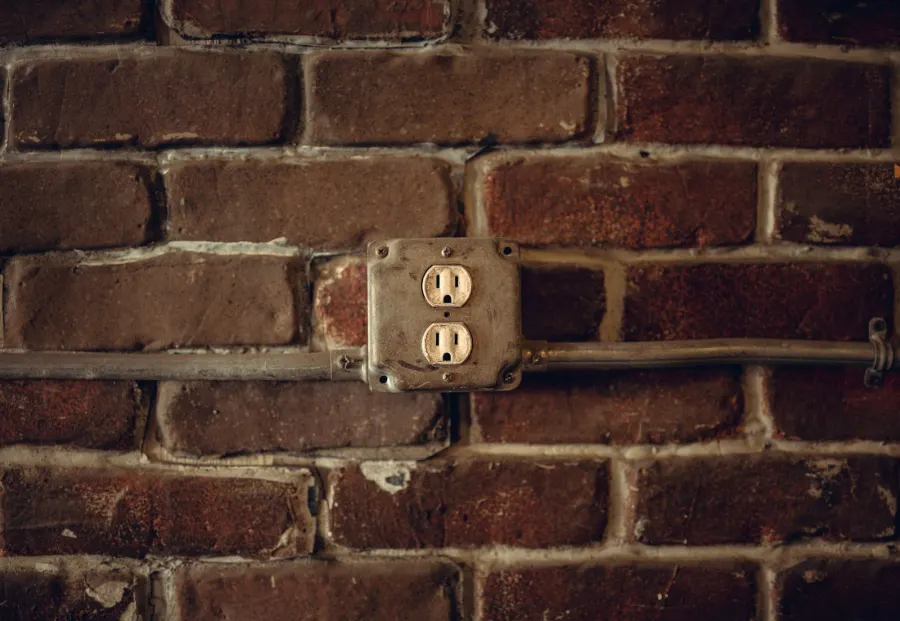 Old two-outlet box on an exposed red brick wall, fed by metal conduit running along the bricks