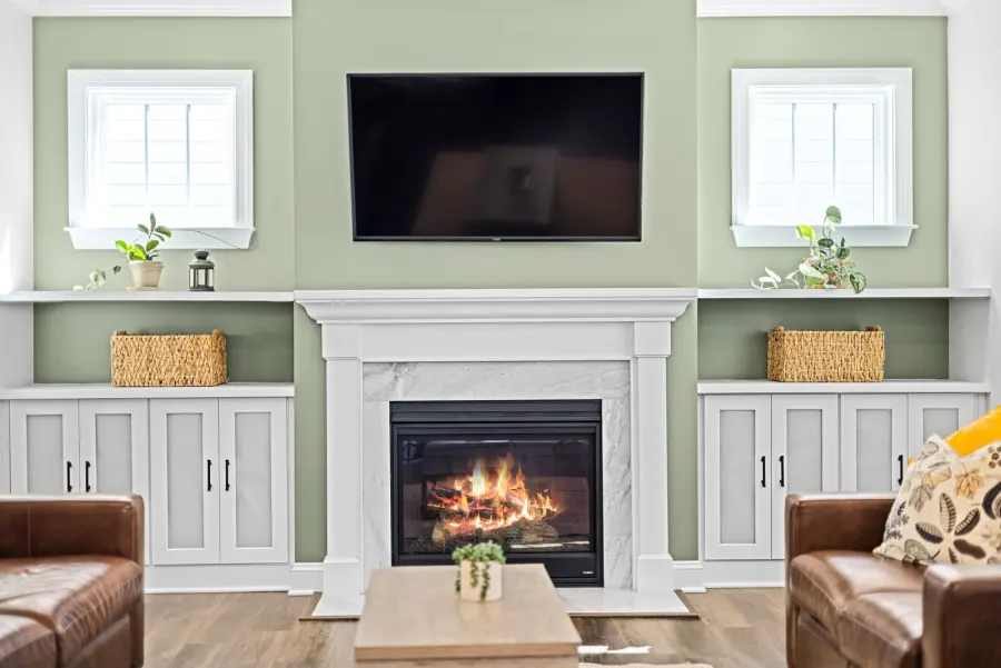 Living room with a flat-screen TV on a green wall above a white fireplace mantel, with built-in cabinets on each side