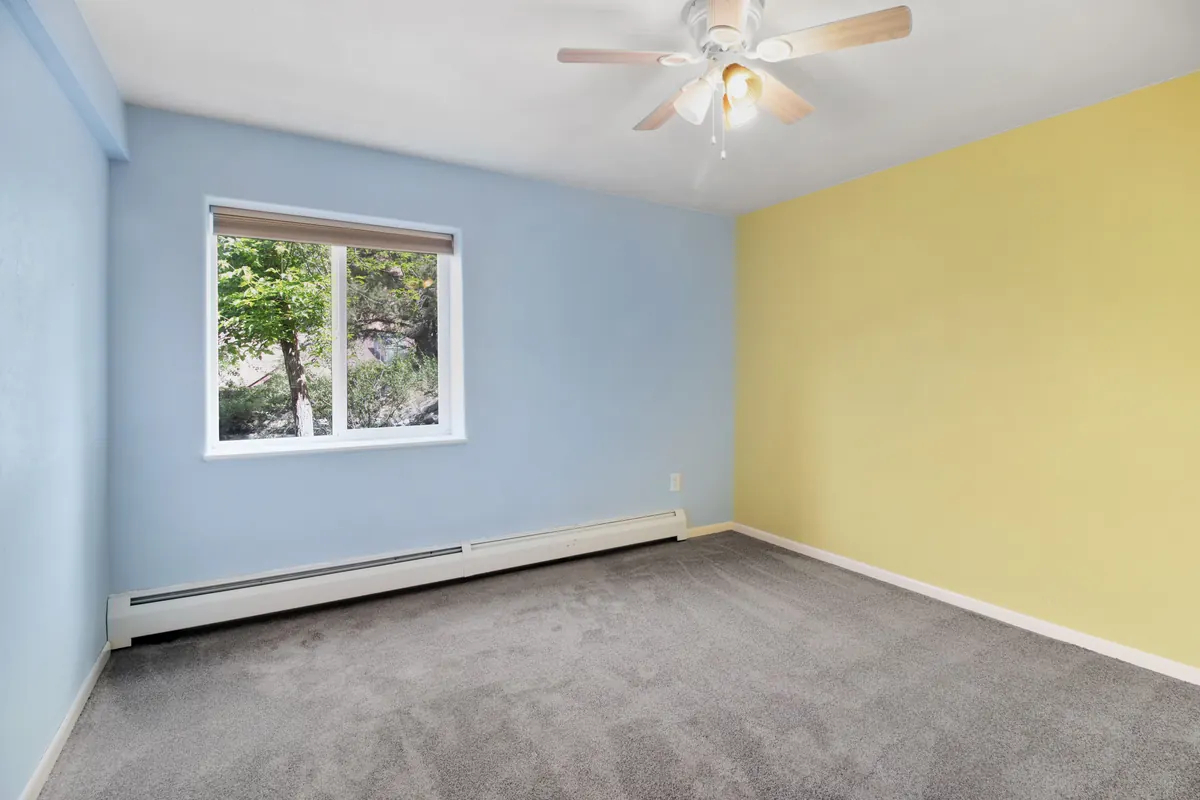 Empty bedroom with blue and yellow walls and a white baseboard heater along the wall under the window