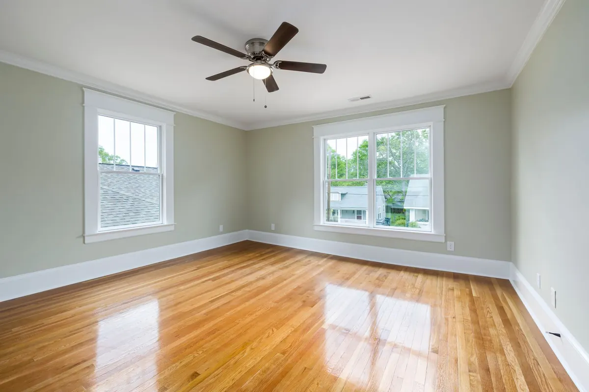 Empty room with wood floors and two windows, a five-blade ceiling fan with a light kit in the middle of the ceiling