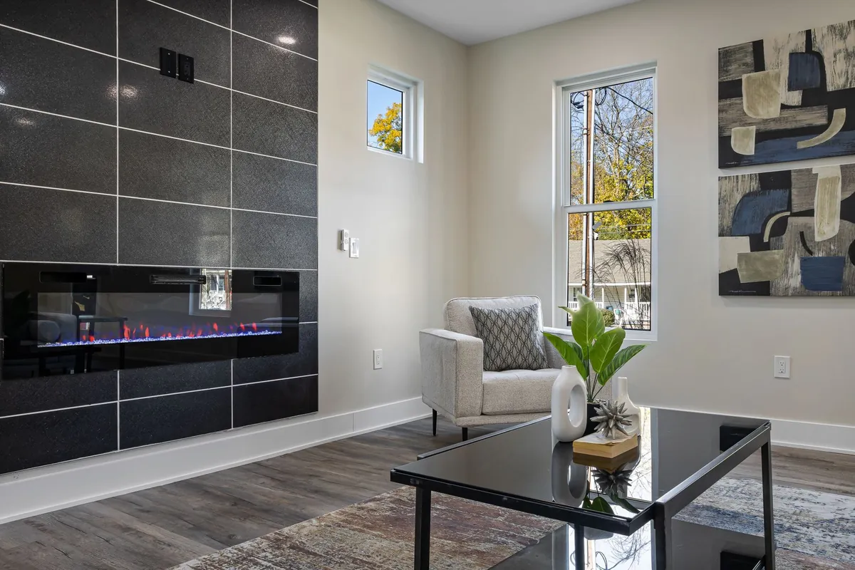 Living room with a long, narrow fireplace glowing in a dark tiled feature wall, an armchair and a glass coffee table in front
