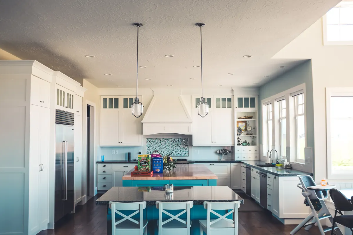 Bright kitchen with rows of small recessed lights in a white ceiling and two pendant lights over a blue island
