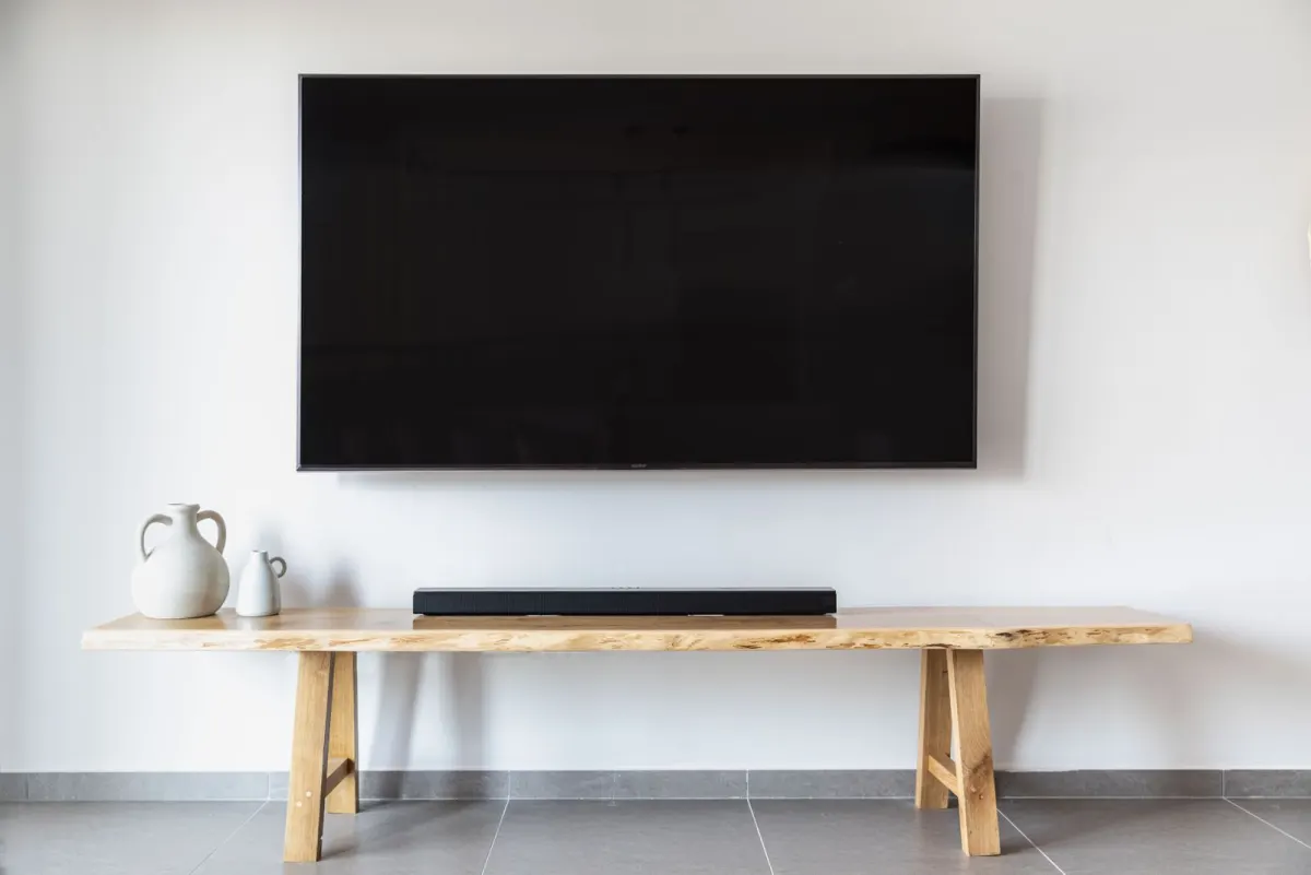 Flat-screen TV mounted on a white wall above a wooden bench with a soundbar, with no cords showing
